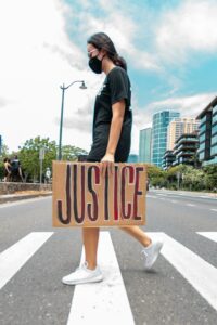 A woman crossing the street holding a cardboard sign that says "justice"